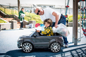 Father and son pose with toy car and groceries on playground.