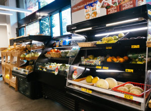 Fresh produce like cantaloupes, mangoes, bell peppers, and pears line refrigerated shelving in Dalda's Community Market. 