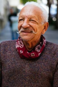 Miguel is smiling, with his handlebar mustache, red scarf/necktie and maroon sweater.