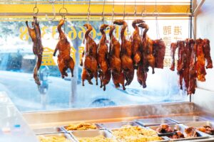 Rows of ducks hang above trays of stir fried noodles, meats, and more.