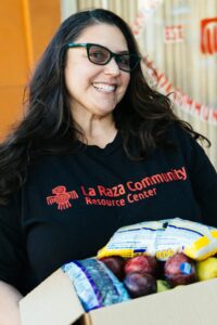 a smiling woman with sunglasses holding a box of produce